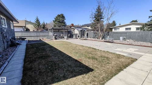 Expansive backyard featuring a manicured lawn, concrete patio, perimeter fencing, a garden shed, and raised garden beds - 3311 108 Street, Edmonton, AB - Outdoor