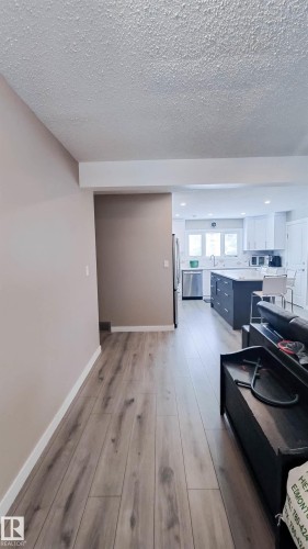Open-concept layout featuring wood-finish flooring, a contemporary kitchen with white cabinetry, a dark-toned island, and stainless steel appliances - 3311 108 Street, Edmonton, AB - Indoor Photo Showing Other Room