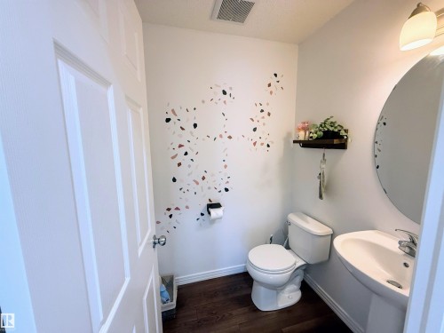 Powder room with wood-finish flooring, pedestal sink, and decorative wall accents - 3538 Claxton Crescent, Edmonton, AB - Indoor Photo Showing Bathroom