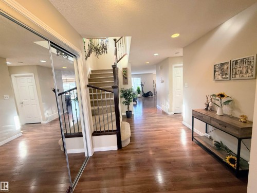 Spacious entryway featuring wood-finish flooring, a carpeted staircase with wrought iron balusters, recessed lighting, and a mirrored sliding closet door - 3538 Claxton Crescent, Edmonton, AB - Indoor Photo Showing Other Room