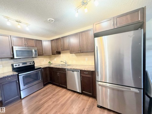 Kitchen featuring rich wood-finish cabinetry, stainless steel appliances, granite-style countertops, and wood-finish flooring - 3538 Claxton Crescent, Edmonton, AB - Indoor Photo Showing Kitchen With Stainless Steel Kitchen
