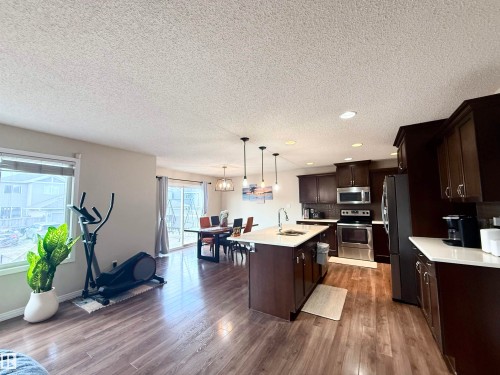 Open-concept living space featuring wood-finish flooring, a kitchen island with seating, dark wood cabinetry, and stainless steel appliances - 3538 Claxton Crescent, Edmonton, AB - Indoor Photo Showing Kitchen With Stainless Steel Kitchen