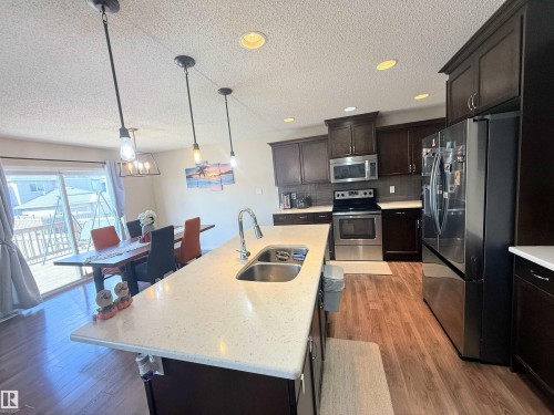 Kitchen featuring dark wood cabinetry, stainless steel appliances, a center island with a double basin sink, light-toned countertops, and wood-finish flooring - 3538 Claxton Crescent, Edmonton, AB - Indoor Photo Showing Kitchen With Stainless Steel Kitchen With Double Sink With Upgraded Kitchen