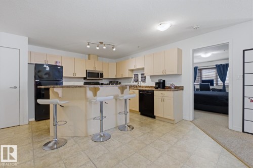 Kitchen featuring light wood-finish cabinetry, black appliances, a stone-finish countertop, and a breakfast bar - 304 4312 139 Ave, Edmonton, AB - Indoor Photo Showing Kitchen