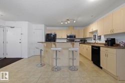 Kitchen featuring a breakfast bar with seating, extensive light wood-finish cabinetry, black appliances, and speckled countertops - 