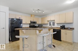 Kitchen featuring light-tone cabinetry, a peninsula with a raised breakfast bar, black appliances, and a track lighting fixture - 