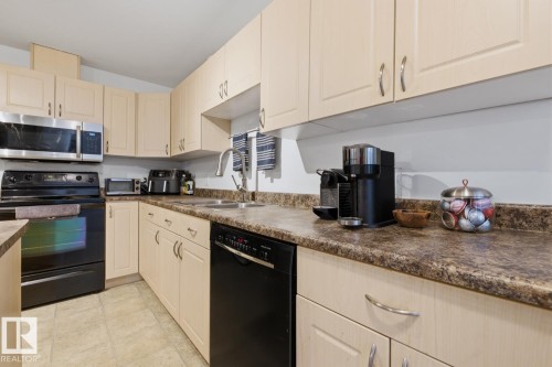 Kitchen featuring light-toned cabinetry, laminate countertops, a stainless steel microwave, and a black oven and dishwasher - 304 4312 139 Ave, Edmonton, AB - Indoor Photo Showing Kitchen With Double Sink