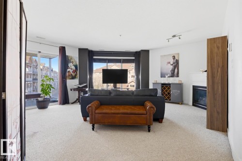 Carpeted living space featuring a built-in fireplace, track lighting, and outdoor balcony access through sliding glass doors - 304 4312 139 Ave, Edmonton, AB - Indoor Photo Showing Living Room With Fireplace