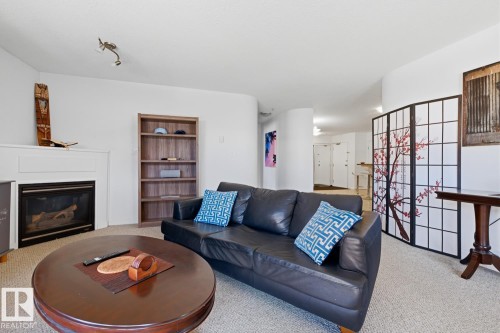 Living area featuring a fireplace with white mantel, light-colored carpet, and a built-in wooden bookshelf - 304 4312 139 Ave, Edmonton, AB - Indoor Photo Showing Living Room With Fireplace