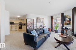 Living area with neutral carpeting, an open concept layout, light-toned kitchen cabinetry, dark appliances, and a glass-paneled patio door - 