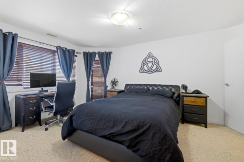 Carpeted bedroom featuring a window with horizontal blinds, a ceiling-mounted light fixture, and a solid white door - 304 4312 139 Ave, Edmonton, AB - Indoor Photo Showing Bedroom