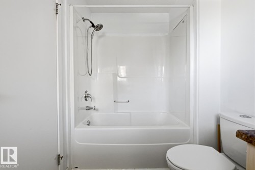White bathtub with an integrated shower surround, featuring chrome fixtures and a handheld showerhead - 304 4312 139 Ave, Edmonton, AB - Indoor Photo Showing Bathroom