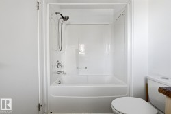 White bathtub with an integrated shower surround, featuring chrome fixtures and a handheld showerhead - 