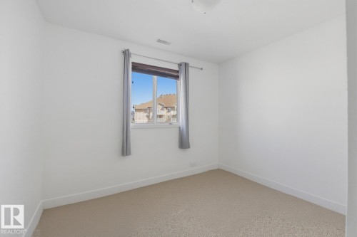 Bright room featuring neutral carpeting, white walls, and a single window with curtain rod and drapes - 304 4312 139 Ave, Edmonton, AB - Indoor Photo Showing Other Room
