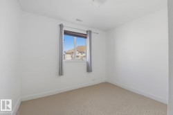 Bright room featuring neutral carpeting, white walls, and a single window with curtain rod and drapes - 