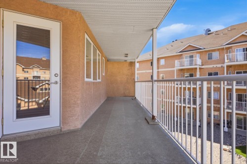 Spacious balcony featuring a textured wall finish, white metal railings, multiple windows, and a full-light entry door - 304 4312 139 Ave, Edmonton, AB - Outdoor With Balcony With Exterior