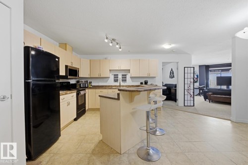 Kitchen featuring wood-finish cabinetry, dark countertops, and tile flooring - 304 4312 139 Ave, Edmonton, AB - Indoor Photo Showing Kitchen