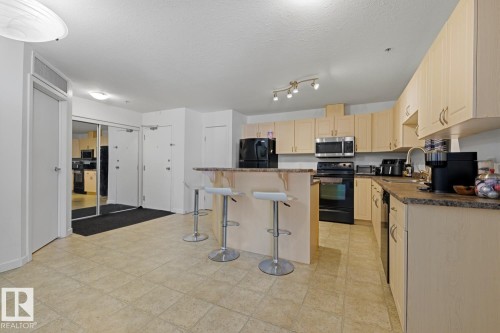 Kitchen featuring light wood-finish cabinetry, black appliances, track lighting, and a breakfast bar with stone-finish countertops - 304 4312 139 Ave, Edmonton, AB - Indoor Photo Showing Kitchen
