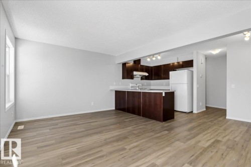 Open-concept living space featuring wood-finish flooring, a kitchen island with seating, dark wood cabinetry, a white tile backsplash, and track lighting - #7 18004 89 St Nw, Edmonton, AB - Indoor Photo Showing Kitchen