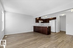 Open-concept living space featuring wood-finish flooring, a kitchen island with seating, dark wood cabinetry, a white tile backsplash, and track lighting - 