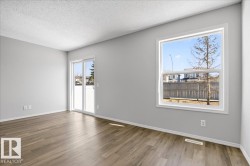 Spacious room featuring wood-finish flooring, light gray painted walls, a large casement window, and a sliding glass door - 