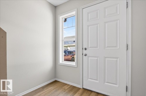 White paneled door with polished hardware, white trim, wood-finish flooring, and a single pane window - #7 18004 89 St Nw, Edmonton, AB - Indoor Photo Showing Other Room