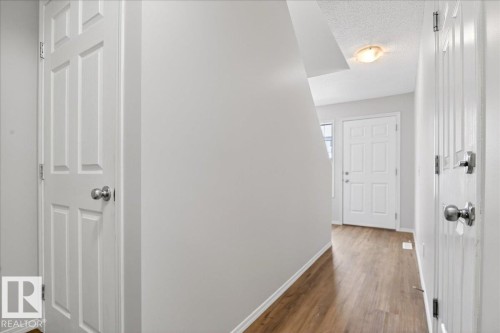 Inviting entryway featuring wood-finish flooring, light grey wall paint, white trim, and a white paneled front door with sidelight - #7 18004 89 St Nw, Edmonton, AB - Indoor Photo Showing Other Room