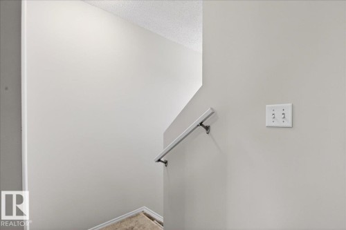 Staircase featuring a white handrail with dark wall mounts, light gray painted walls, and a popcorn ceiling texture - #7 18004 89 St Nw, Edmonton, AB - Indoor