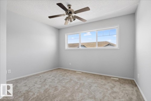 Spacious room featuring neutral carpeting, light gray walls, a multi-pane window, white baseboards, and a ceiling fan with light fixture - #7 18004 89 St Nw, Edmonton, AB - Indoor Photo Showing Other Room