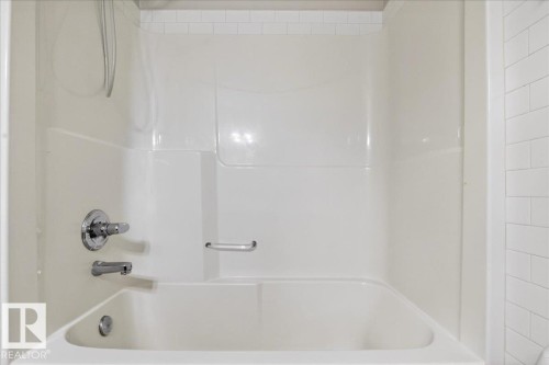 White bathtub with integrated shower surround, chrome fixtures, and a recessed soap dish - #7 18004 89 St Nw, Edmonton, AB - Indoor Photo Showing Bathroom