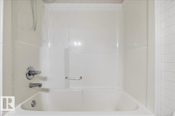 White bathtub with integrated shower surround, chrome fixtures, and a recessed soap dish - 