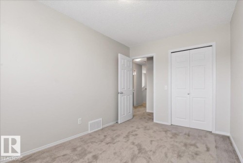 Light gray painted walls, textured ceiling, light gray carpet, white baseboards, and white bi-fold closet doors - #7 18004 89 St Nw, Edmonton, AB - Indoor Photo Showing Other Room
