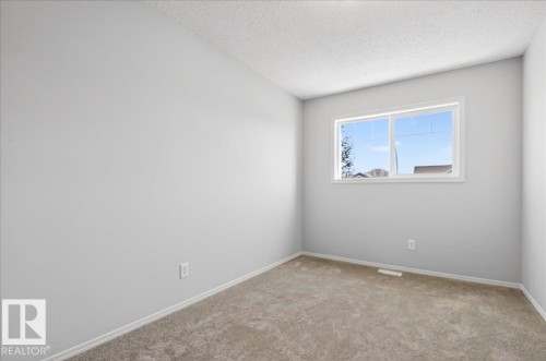 Neutral-toned room featuring a large window with white trim, light gray walls, and textured carpeting - #7 18004 89 St Nw, Edmonton, AB - Indoor Photo Showing Other Room