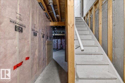 Unfinished basement featuring a wooden staircase with a painted white handrail, exposed wood framing, concrete foundation walls, and insulated wall sections - #7 18004 89 St Nw, Edmonton, AB - Indoor Photo Showing Other Room