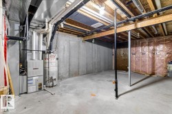 Unfinished basement featuring concrete walls and flooring, exposed ceiling joists, an HVAC system, and a water heater - 