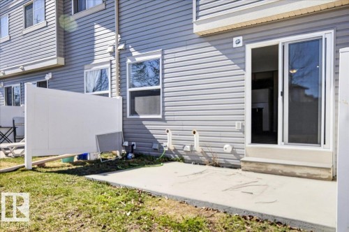 Rear exterior featuring a concrete patio, white vinyl privacy fence, gray horizontal siding, and multiple windows - #7 18004 89 St Nw, Edmonton, AB - Outdoor