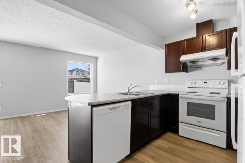 Kitchen featuring wood-finish flooring, dark wood cabinetry, light-toned countertops, white appliances, and a double basin sink - #7 18004 89 St Nw, Edmonton, AB - Indoor Photo Showing Kitchen With Double Sink