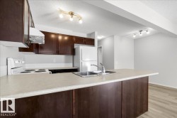 Kitchen featuring a peninsula with integrated sink, dark wood-finish cabinetry, light-toned countertops, and a white tile backsplash - 