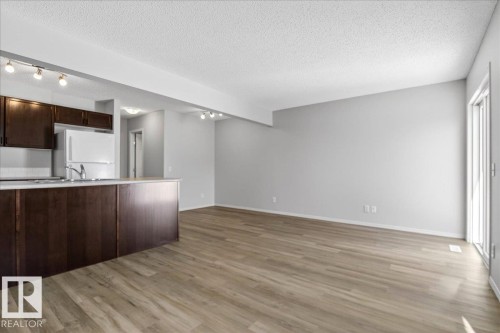 Open-concept living space featuring wood-finish flooring, light gray wall paint, and a kitchen island with dark wood cabinetry - #7 18004 89 St Nw, Edmonton, AB - Indoor Photo Showing Kitchen