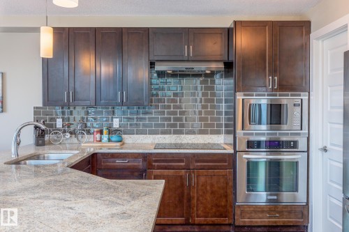 Kitchen featuring dark wood cabinetry, light-toned countertops, and a reflective subway tile backsplash - 513 1230 Windermere Way, Edmonton, AB 