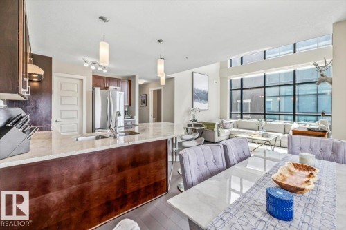 Open-concept living area featuring dark wood-finish flooring, a kitchen with stainless steel appliances and dark cabinetry, and a granite countertop island - 513 1230 Windermere Way, Edmonton, AB 