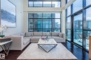 Living area featuring soaring two-story windows with dark framing, rich wood-finish flooring, and a private balcony with glass railing - 513 1230 Windermere Way, Edmonton, AB 
