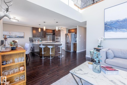 Open-concept living space featuring high ceilings, wood-finish flooring, and a modern kitchen - 513 1230 Windermere Way, Edmonton, AB 