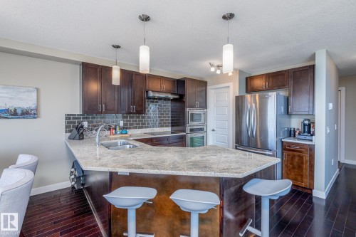 Kitchen featuring dark wood-finish cabinetry, a light-toned speckled countertop, and a dark subway tile backsplash - 513 1230 Windermere Way, Edmonton, AB 