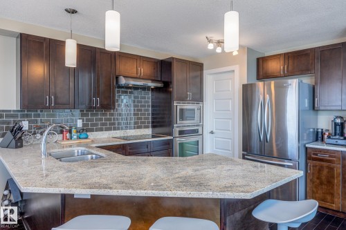 Kitchen featuring a U-shaped peninsula with a double basin sink, light-toned countertops, and dark wood cabinetry - 513 1230 Windermere Way, Edmonton, AB 