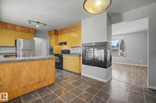 Kitchen featuring dark tile flooring, a wood-paneled island with a stone-finish countertop, and yellow cabinetry with a tile backsplash - 6048 105B Street, Edmonton, AB - Indoor Photo Showing Kitchen