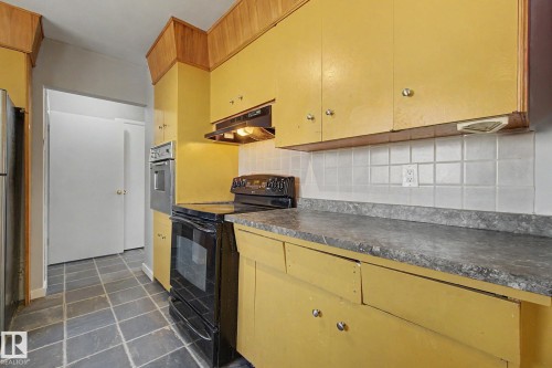 Kitchen featuring wood-finish flooring, yellow cabinetry, a built-in oven, and a black range - 6048 105B Street, Edmonton, AB - Indoor Photo Showing Kitchen