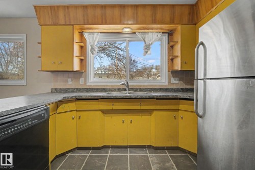 Kitchen featuring yellow cabinetry, dark gray countertops, a stainless steel refrigerator, and dark tile flooring - 6048 105B Street, Edmonton, AB - Indoor Photo Showing Kitchen With Double Sink