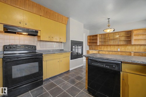 Kitchen featuring a fireplace with a black iron insert, dark square floor tiles, and upper and lower cabinetry - 6048 105B Street, Edmonton, AB - Indoor Photo Showing Kitchen