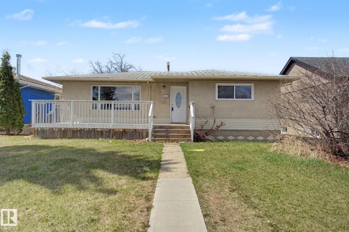 Stucco exterior residence featuring a front deck with white railings, a concrete walkway, and a front entry door with an oval glass insert - 6048 105B Street, Edmonton, AB - Outdoor With Deck Patio Veranda